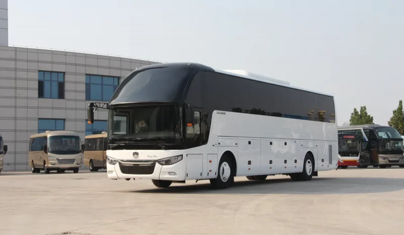 Маршрутки (не) лучше? Китайские автобусы на трассе из Гродно в Минск взволновали гродненцев Гладкий белый туристический автобус, напоминающий китайские автобусы Zhongtong LCK6127H в Беларуси, припаркован на бетонной стоянке, на заднем плане вырисовывается современное здание.